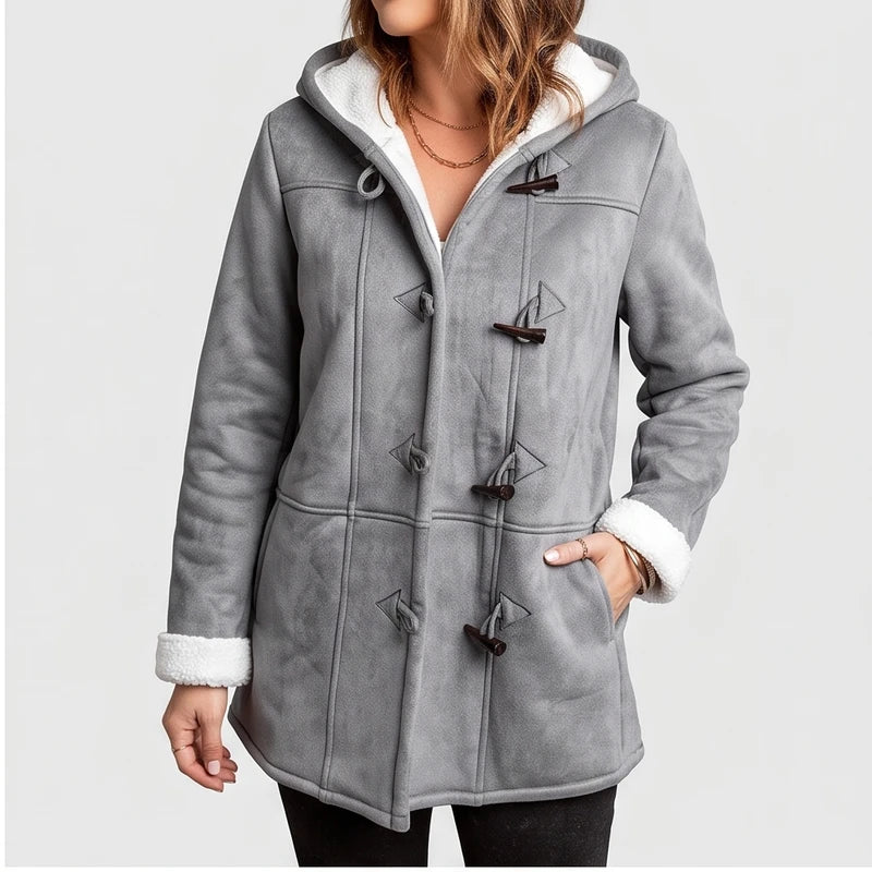 Woman wearing a grey hooded coat with visible white borg lining, dark toggle closures, and her hands in pockets.