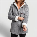 Woman wearing a gray hooded coat with white borg lining visible at the cuffs and hood, featuring brown toggle closures.