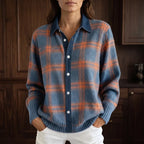Woman wearing a blue and orange plaid knit cardigan over a denim shirt, with her hands in white pants pockets.
