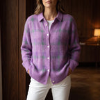 Woman wearing a purple and green plaid knit cardigan with white buttons, hands in pockets, over white pants.