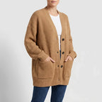 Woman wearing an oversized camel chunky knit button-down cardigan with front pockets over a white tee and blue jeans.
