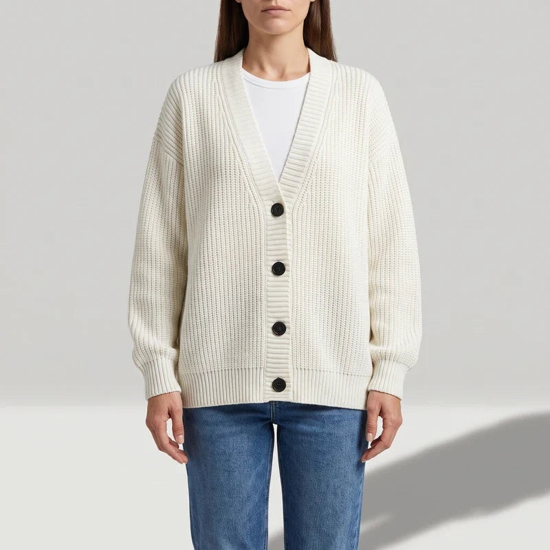 Woman wearing a cream-colored chunky knit cardigan with ribbed texture, black buttons, and a V-neck over a white t-shirt and blue jeans.