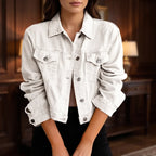 Woman wearing an unbuttoned light beige cropped denim jacket with chest pockets and silver buttons, over dark pants.