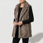 Woman wearing a long, mottled brown and grey faux fur vest with wide lapels over a black long-sleeved shirt.