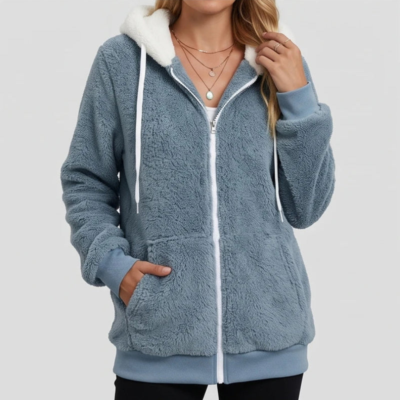 Woman wearing a blue-grey fuzzy fleece hoodie with a white zipper, white drawstring, and a white sherpa-lined hood.