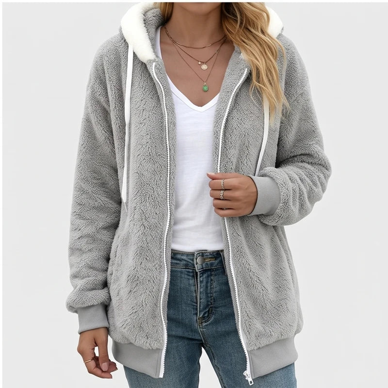 Woman wearing an open gray fuzzy zip-up hoodie with a white hood lining, paired with a white t-shirt and blue jeans.