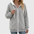 Woman wearing an open gray fuzzy zip-up hoodie with a white hood lining, white drawstrings, and ribbed cuffs.