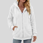 Woman wearing a fuzzy white fleece zip-up hoodie with a hood and white drawstrings, hand in pocket.