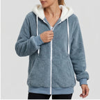 Woman zipping up a cozy blue fleece hoodie with a white sherpa-lined hood, white drawstring, and front pockets.