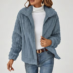 Woman wearing a blue textured fleece zip-up jacket over a white turtleneck and blue jeans with a brown belt.