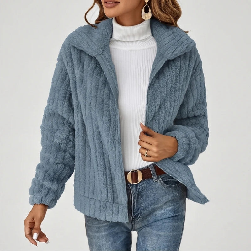 Woman wearing a blue textured fleece zip-up jacket over a white turtleneck and blue jeans with a brown belt.