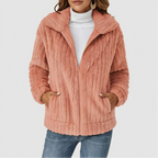 Woman wearing a fuzzy peach-colored fleece zip-up jacket over a white turtleneck, hands in pockets.