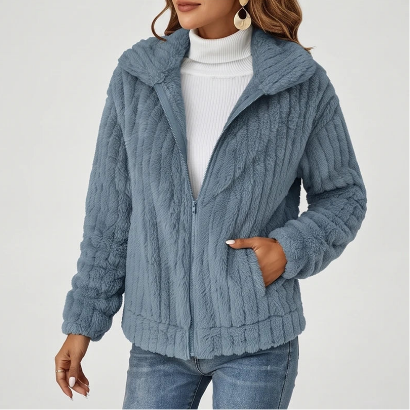 Woman wearing an open light blue fleece jacket with vertical ribbing, a high collar, zipper, and pockets, over a white turtleneck.