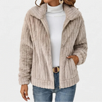 Woman wearing a beige ribbed fuzzy zip-up jacket with a wide collar, light blue jeans, and a white turtleneck top.