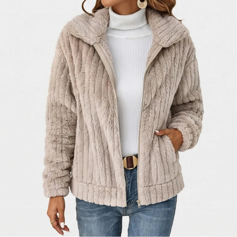 Woman wearing a beige ribbed fuzzy zip-up jacket with a wide collar, light blue jeans, and a white turtleneck top.