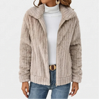 Woman wearing an open light beige ribbed fuzzy jacket over a white turtleneck, blue jeans, and a brown belt.