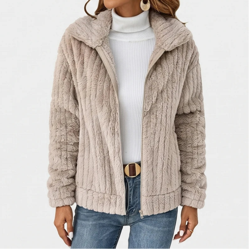 Woman wearing an open light beige ribbed fuzzy jacket over a white turtleneck, blue jeans, and a brown belt.