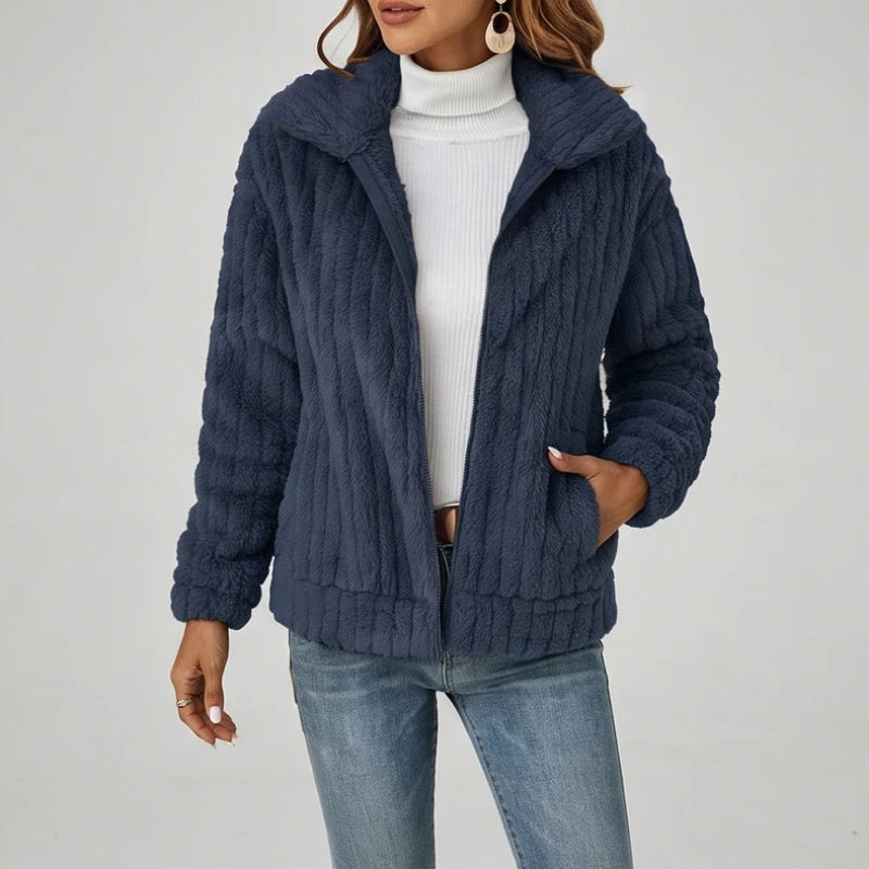 Woman wearing an open navy blue ribbed fleece zip-up jacket over a white turtleneck, with hands in pockets.