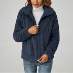 Woman wearing a dark blue textured fleece zip-up jacket over a white turtleneck and light wash jeans.