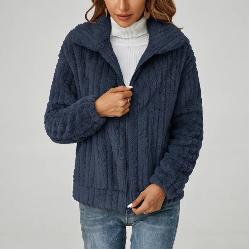 Woman wearing a dark blue textured fleece zip-up jacket over a white turtleneck and light wash jeans.