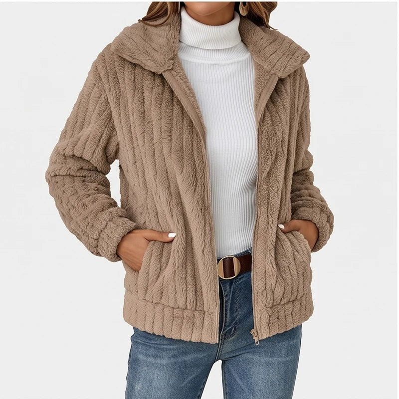Woman wearing a textured tan fleece zip-up jacket with a collar, over a white ribbed turtleneck and blue jeans.