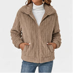 Woman wearing a partially unzipped, tan ribbed fleece jacket with a wide collar, front pockets, and blue jeans.