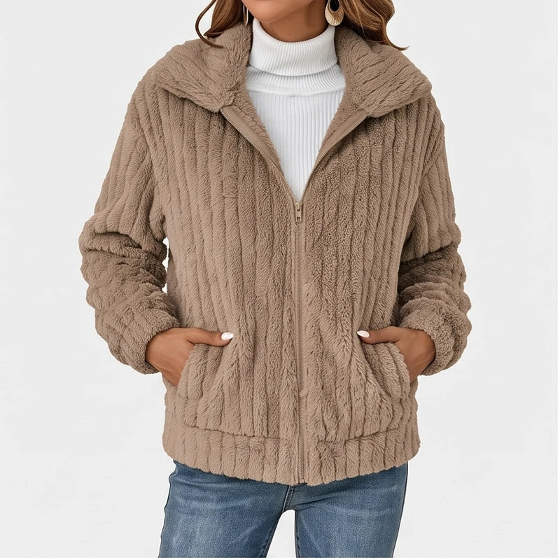 Woman wearing a partially unzipped, tan ribbed fleece jacket with a wide collar, front pockets, and blue jeans.