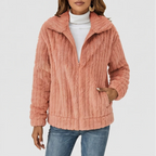 Woman wearing a textured dusty rose plush zip-up jacket over a white turtleneck and blue jeans, hand in pocket.