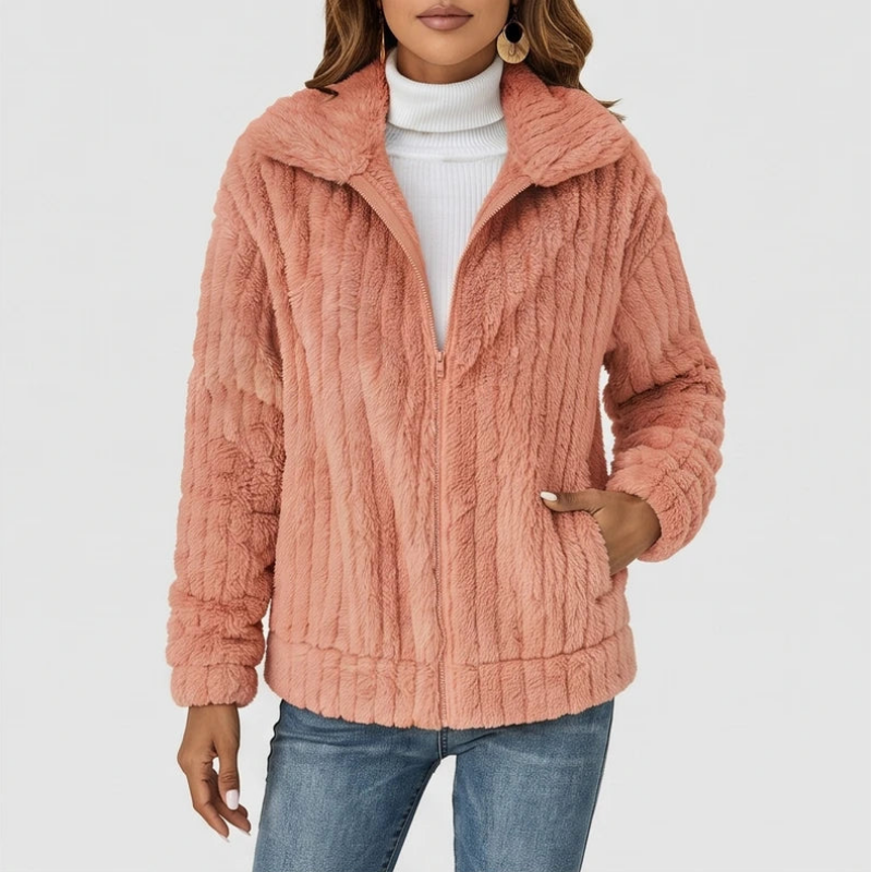 Woman wearing a textured dusty rose plush zip-up jacket over a white turtleneck and blue jeans, hand in pocket.