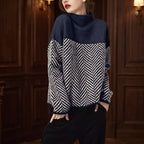 Woman wearing a navy and cream herringbone sweater with a high roll neck, posing with hands in pockets.