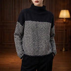 Woman wearing a black and white herringbone pattern jumper with a solid black roll neck and dark trousers.
