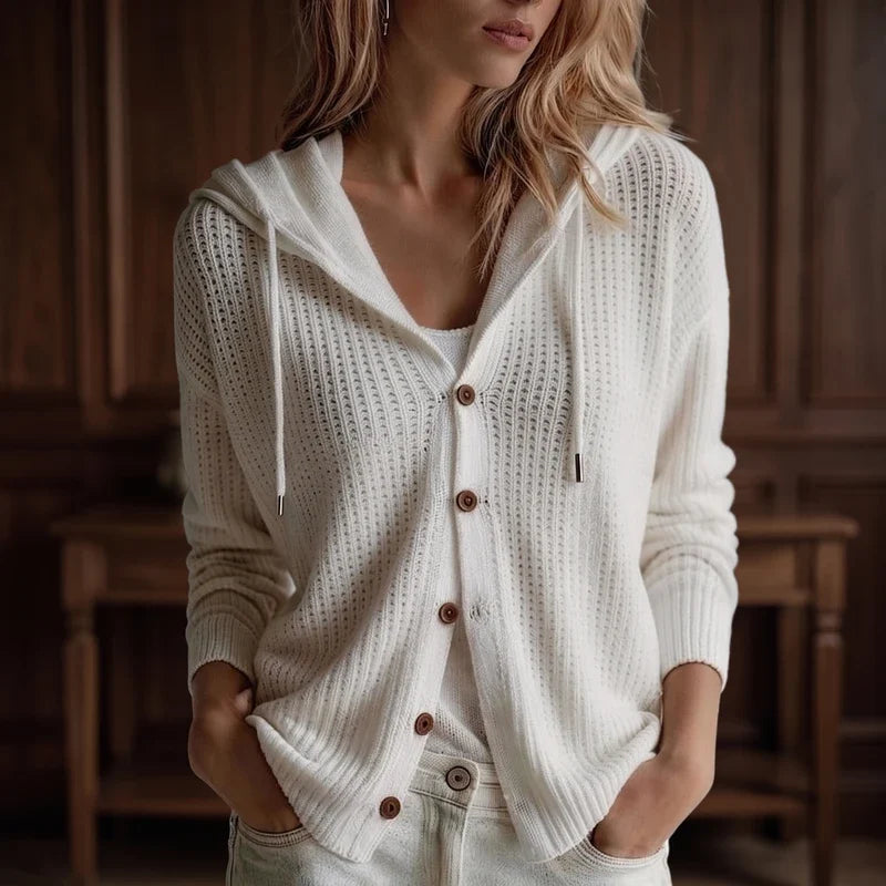 Woman wearing a relaxed-fit, cream knit hooded cardigan with brown buttons and drawstrings, hands in light denim pockets.