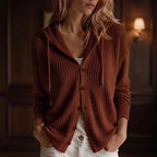 Woman wearing an open, rusty brown knit hooded cardigan with five buttons over a white top and light jeans.