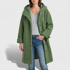 Woman wearing a long, textured green hooded coat over a gray V-neck tee and blue jeans.