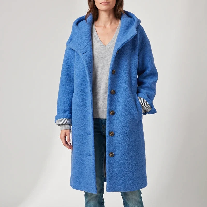 Woman wearing a vibrant blue textured long hooded coat with large brown buttons and rolled-up striped cuffs.