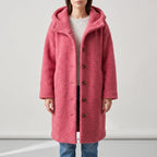 Woman wearing a long, hooded, textured pink coat with visible brown buttons over a light sweater and jeans.