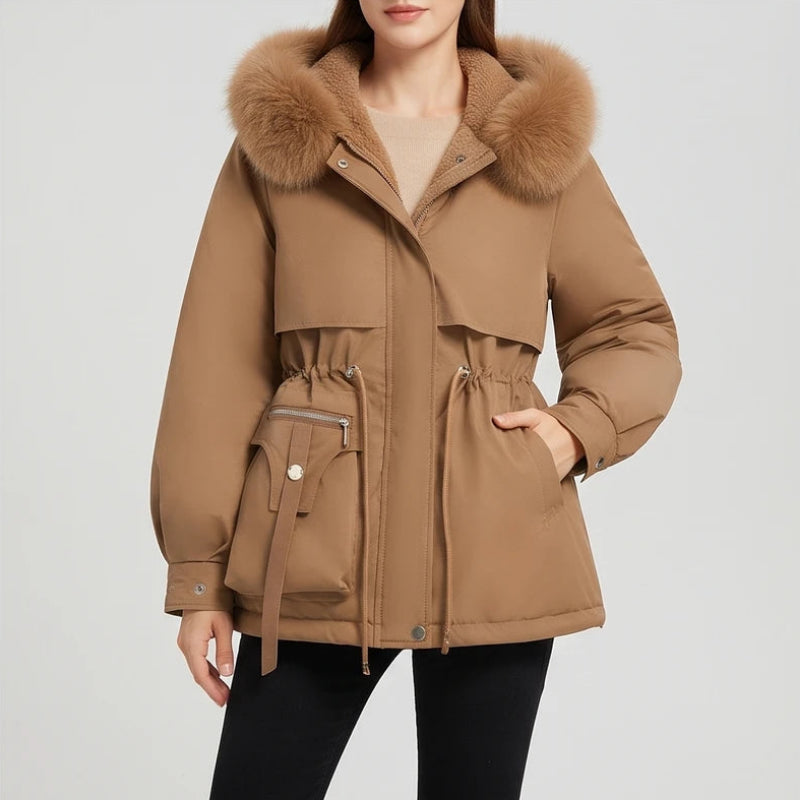 Woman wearing a warm brown parka with a fluffy faux fur-trimmed hood, cinched waist, and zippered pocket.