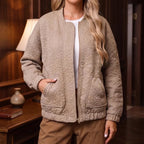 Woman wearing a beige quilted bomber jacket with floral pattern, zippered front, and elastic cuffs, standing indoors.