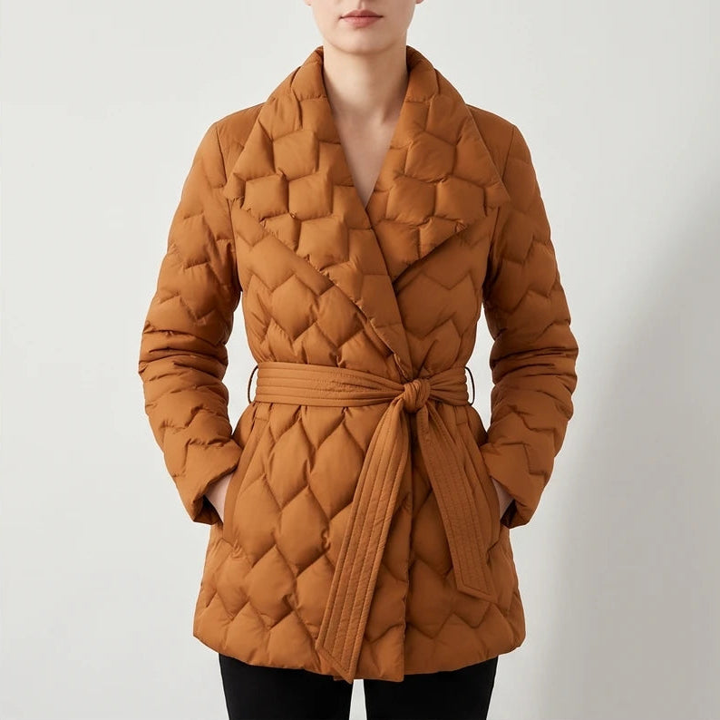 Woman wearing a rust-colored quilted puffer coat with a wide collar, tied at the waist, hands in pockets.