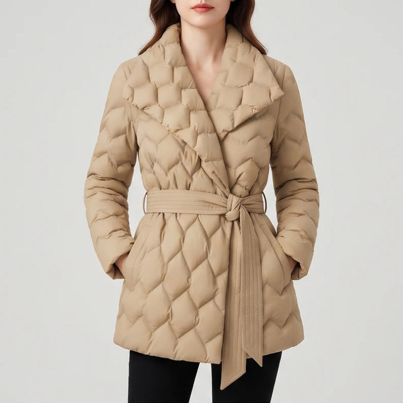 Woman wearing a beige quilted puffer coat with a wide lapel collar, tied belt, and hands in pockets on a plain white background.