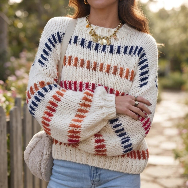 Woman wearing a cream chunky knit jumper with red, orange, and navy textured stripes over light blue jeans.