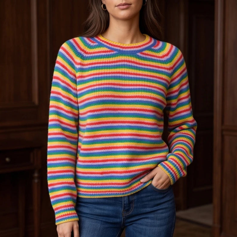 Woman wearing a colorful rainbow-striped knit jumper with a crew neck and raglan sleeves, hand in blue jeans pocket.