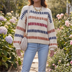 Woman wearing a cream chunky knit jumper with horizontal stripes in navy, rust, and red, standing in a garden.