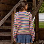 Woman facing away, wearing a rainbow striped knit sweater with puffy sleeves and a blue pleated denim skirt.