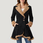 Woman wearing a black suede coat with a tan faux fur collar, cuffs, and asymmetric hem, hands in pockets.