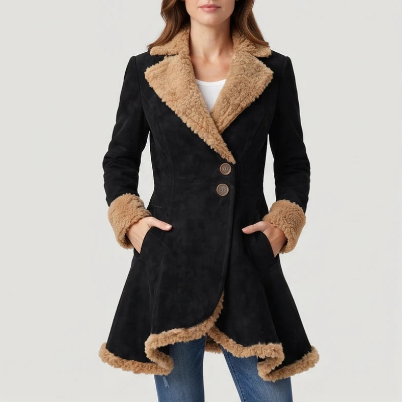 Woman wearing a black suede coat with a tan faux fur collar, cuffs, and asymmetric hem, hands in pockets.