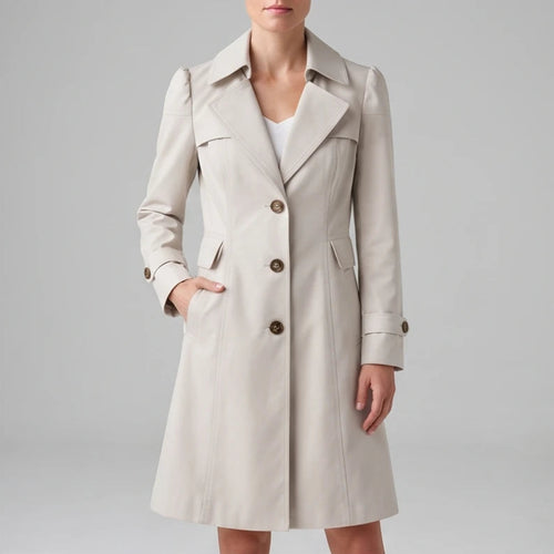 Woman wearing a light beige trench coat with prominent lapels, dark brown buttons, and one hand in a pocket.