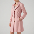 Woman wearing a long, light pink trench coat with brown buttons, a classic collar, and one hand in a side pocket.
