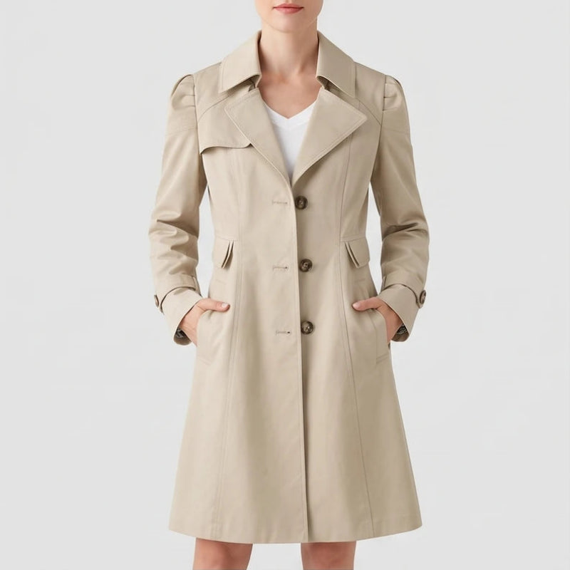 Woman wearing a beige trench coat with puff shoulders, brown buttons, and hands in the side pockets, against a white background.