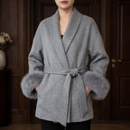 Woman wearing a gray wool coat with a wide lapel, tied waist, and luxurious gray fur cuffs.